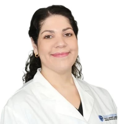 Smiling female healthcare professional in a white coat, facing the camera, isolated on white background with a subtle logo on the coat pocket.