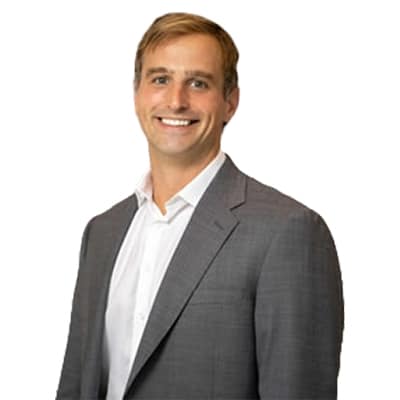 Portrait of a smiling man in a gray suit and white shirt, posed against a plain white background by default.