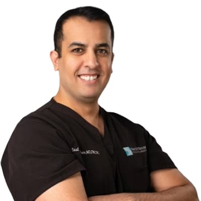 Smiling medical professional in black scrubs with arms crossed, posing against a white background.