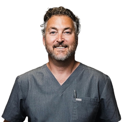 Smiling male medical professional wearing gray scrubs against a white background.