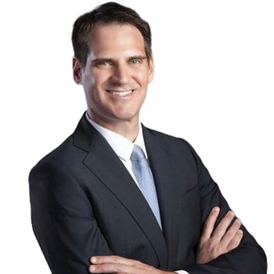 Professional portrait: smiling man in a dark suit with arms crossed, looking confident and approachable.