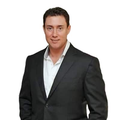 Man in a dark suit and white shirt smiling at the camera.