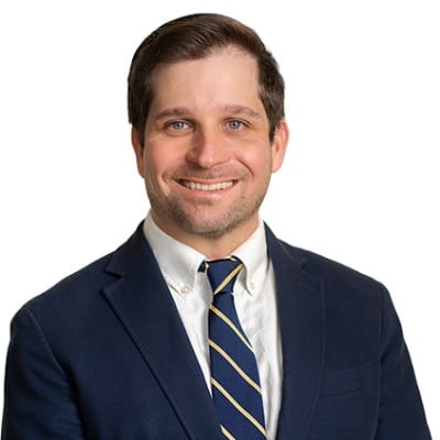 Smiling man in a navy suit and striped tie against a white background, professional headshot