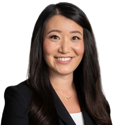 Head-and-shoulders portrait of a smiling Asian woman with long dark hair, wearing a black blazer and white top.
