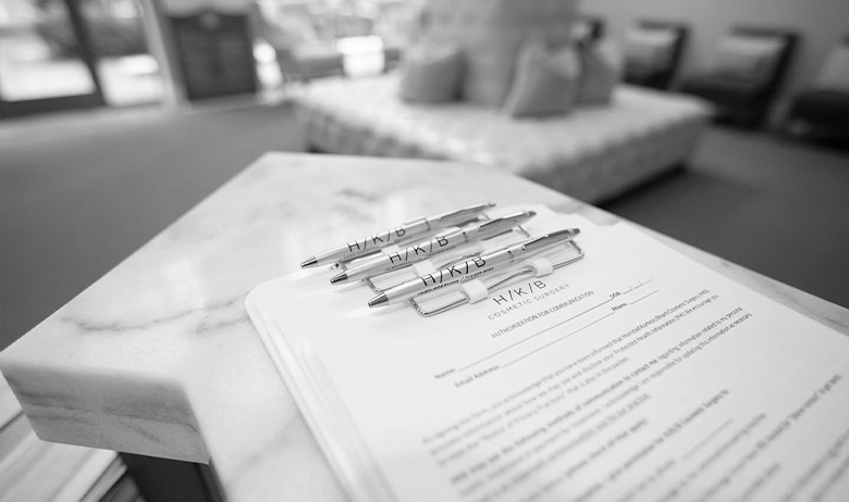 Pens labeled HYKB resting on a contract or form on a marble desk, with a blurred seating area in the background.