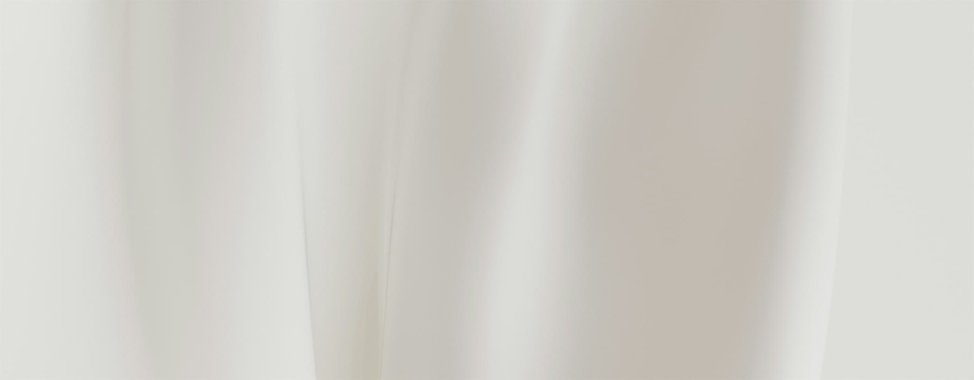 Close-up of pale cream curtains with soft vertical folds and gentle lighting.